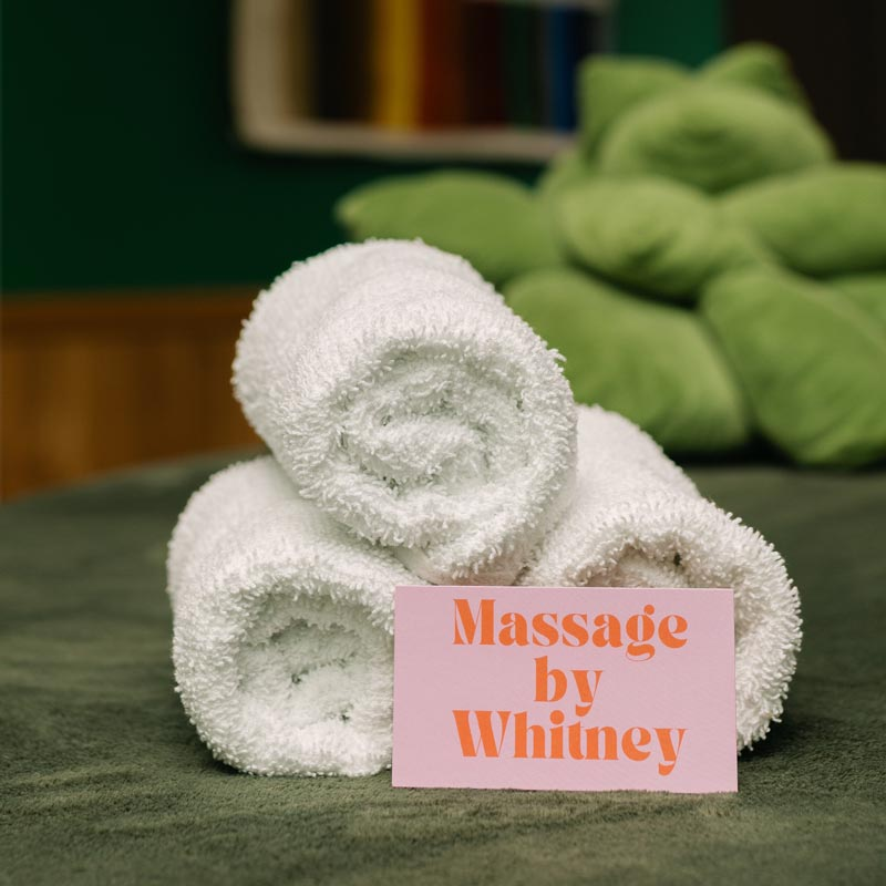 Massage by Whitney business card on massage table with rolled towels.